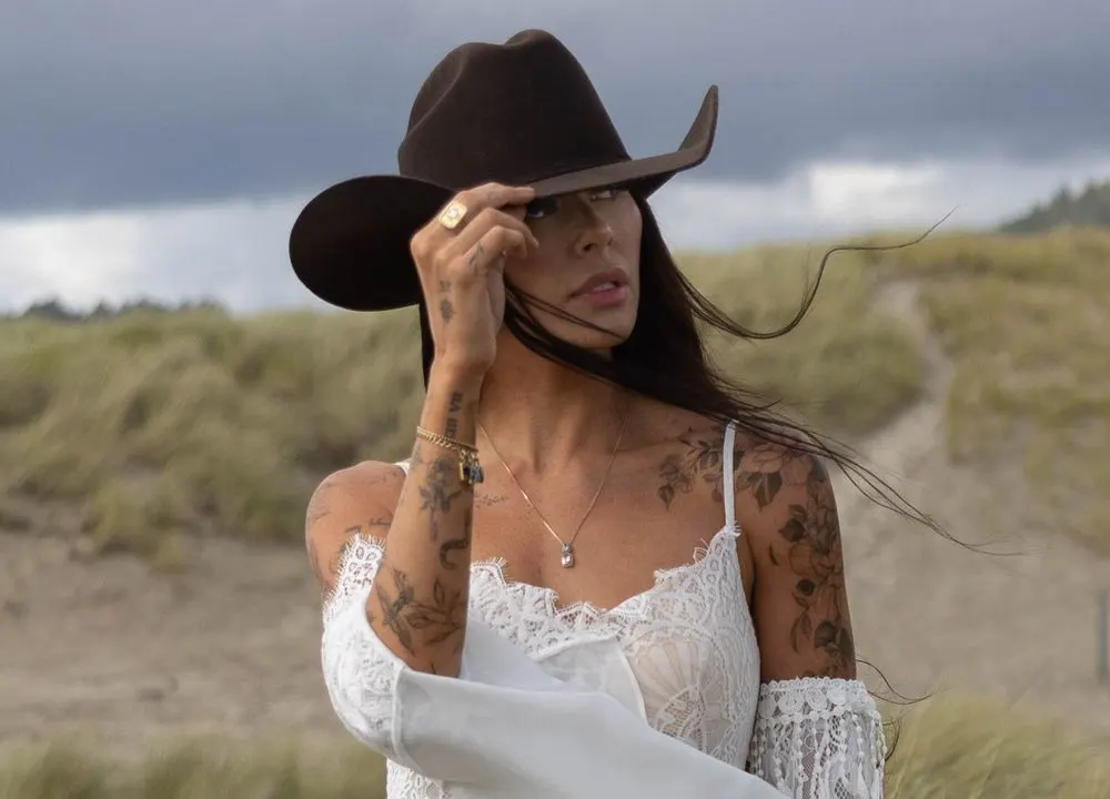 A bride in a cowboy hat among coastal dunes